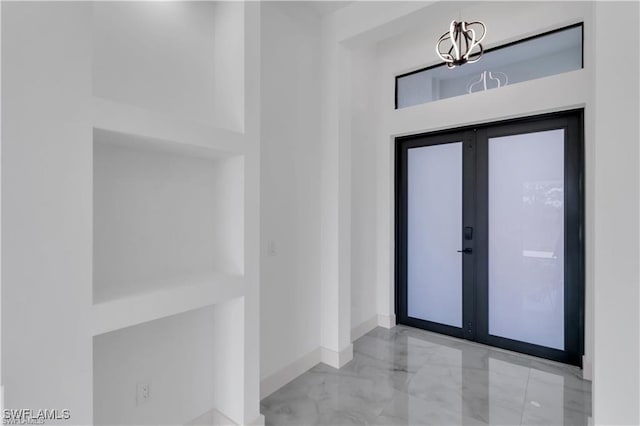 foyer featuring french doors, marble finish floor, baseboards, and a notable chandelier