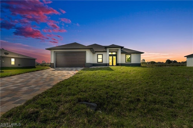 prairie-style home with a front yard, a garage, decorative driveway, and stucco siding