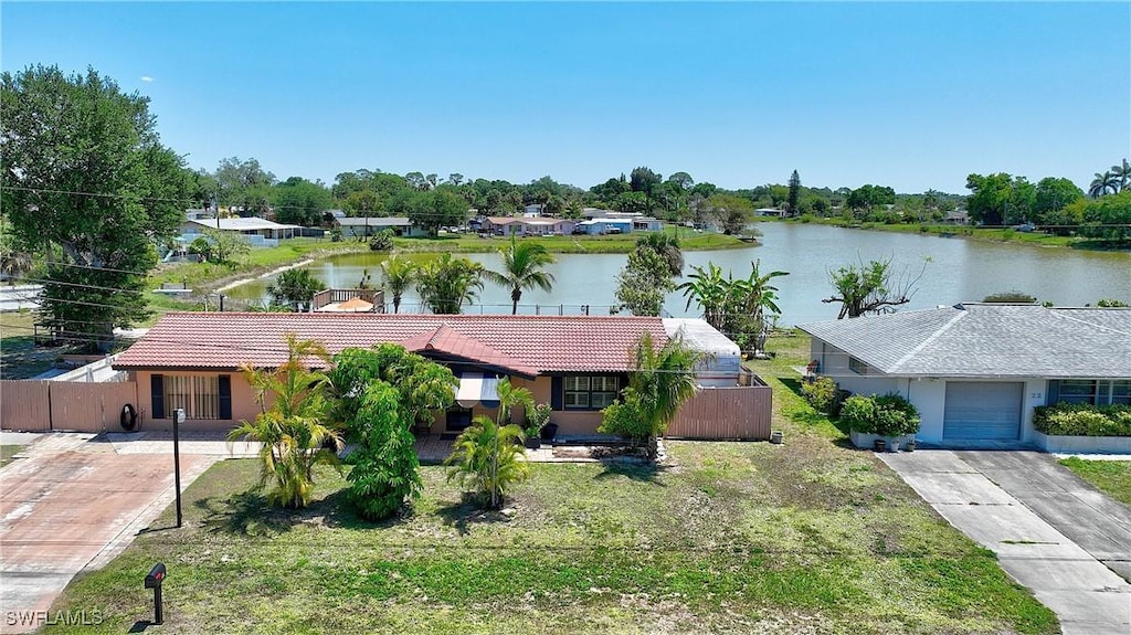 view of front facade with a tile roof, a water view, driveway, fence, and stucco siding