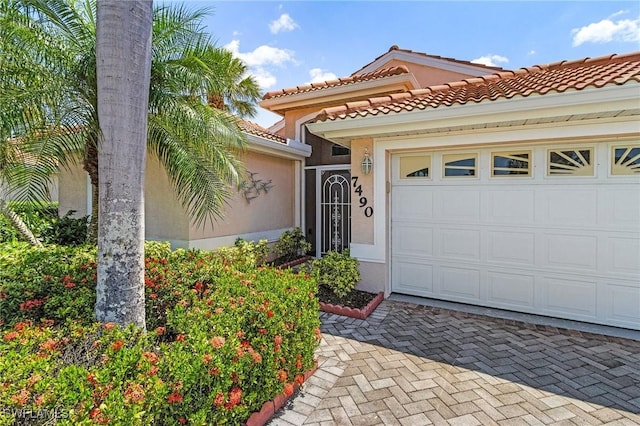 property entrance featuring a tiled roof, an attached garage, decorative driveway, and stucco siding