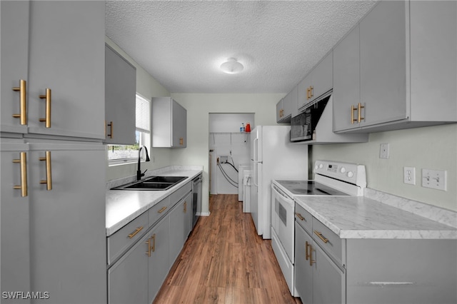 kitchen with white appliances, a sink, gray cabinets, light countertops, and wood finished floors