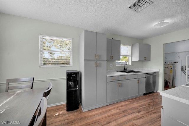 kitchen with gray cabinetry, stainless steel dishwasher, a sink, wood finished floors, and a textured ceiling