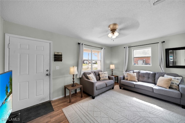living room featuring light wood-style flooring, a ceiling fan, a textured ceiling, and baseboards