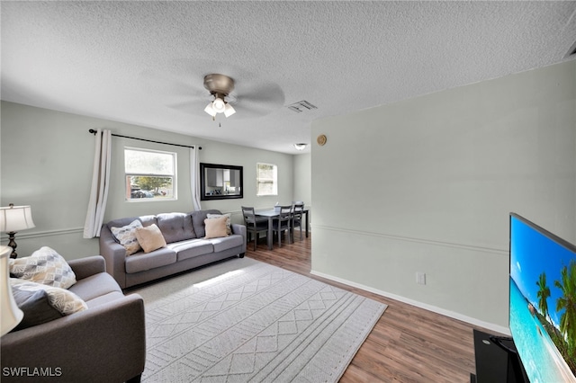 living area featuring ceiling fan, wood finished floors, a textured ceiling, and baseboards