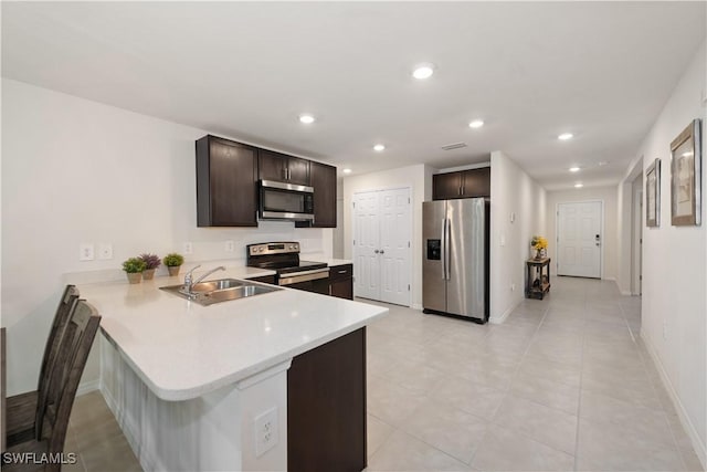 kitchen featuring a peninsula, light countertops, dark brown cabinets, stainless steel appliances, and a sink