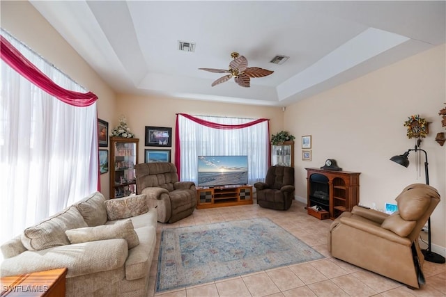 living area featuring a ceiling fan, tile patterned floors, visible vents, and a raised ceiling