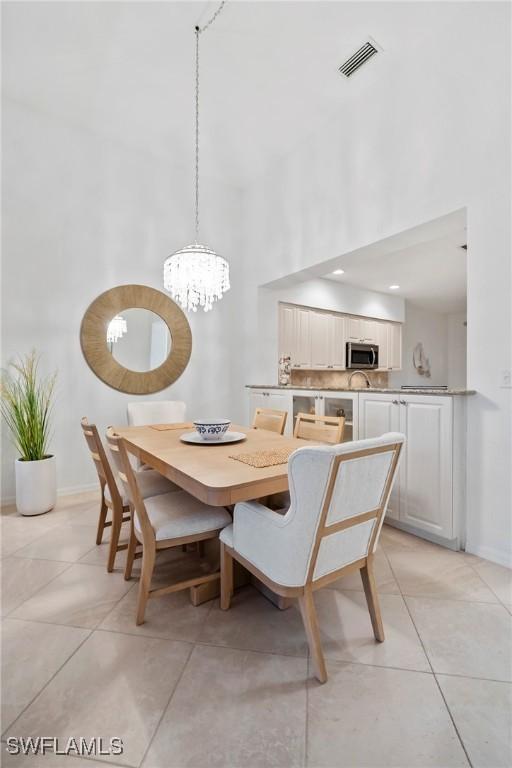 3570 Haldeman Creek Dr Unit 134, Naples, FL 34112 - dining room featuring light tile patterned floors, visible vents, a chandelier, a high ceiling, and baseboards