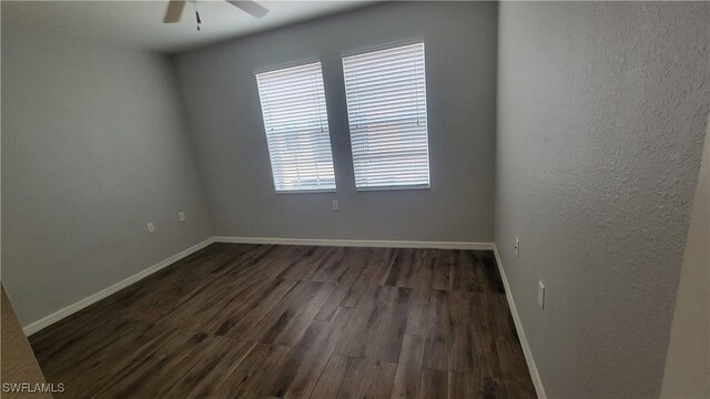 unfurnished room featuring dark wood finished floors, a ceiling fan, and baseboards