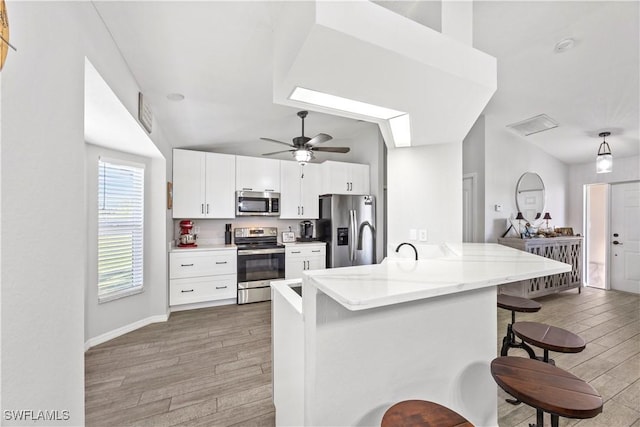 kitchen with white cabinets, light stone counters, wood finished floors, appliances with stainless steel finishes, and a breakfast bar area