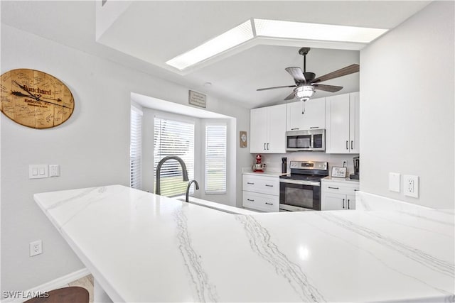 kitchen featuring stainless steel appliances, a peninsula, light stone counters, and a ceiling fan