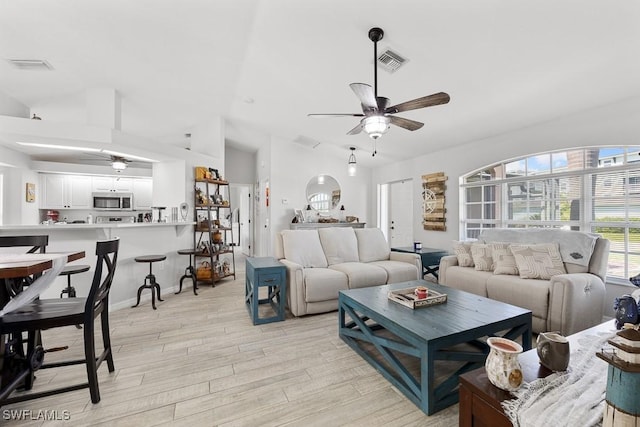 living room featuring vaulted ceiling, a ceiling fan, light wood-style floors, and visible vents