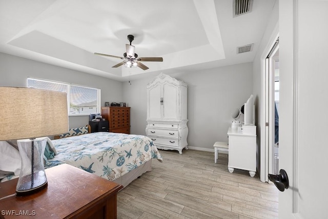 bedroom featuring baseboards, light wood-style floors, visible vents, and a raised ceiling