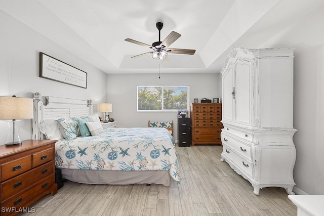 bedroom with light wood finished floors, a tray ceiling, and ceiling fan