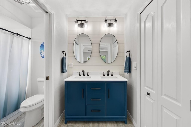 bathroom with toilet, a sink, double vanity, and baseboards