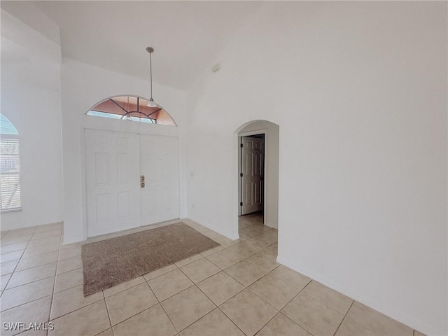 entryway featuring light tile patterned floors, high vaulted ceiling, and arched walkways
