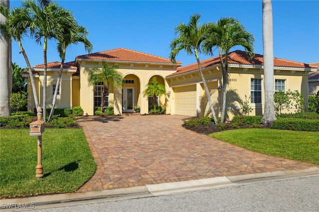 mediterranean / spanish home with a tile roof, decorative driveway, an attached garage, a front yard, and stucco siding