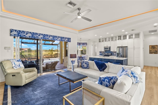living area with a tray ceiling, visible vents, recessed lighting, light wood-style floors, and a ceiling fan