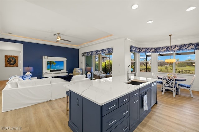 kitchen featuring a kitchen island with sink, light wood-style flooring, stainless steel dishwasher, a sink, and light stone countertops