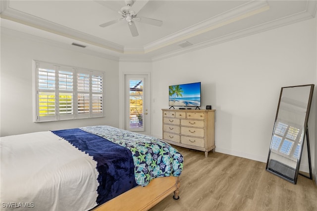 bedroom featuring a raised ceiling, wood finished floors, crown molding, and multiple windows