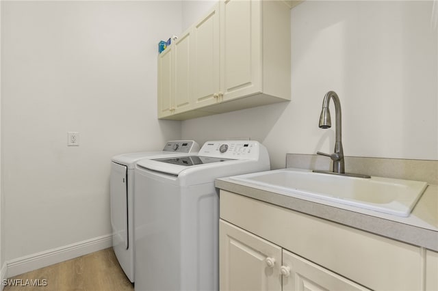 laundry room with a sink, baseboards, separate washer and dryer, cabinet space, and light wood-style flooring