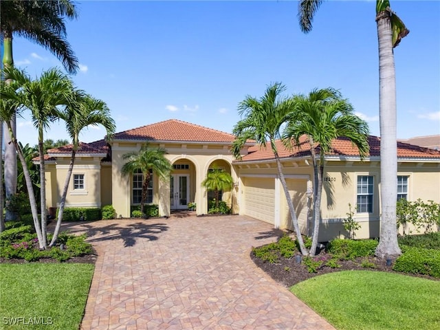 mediterranean / spanish-style house featuring stucco siding, a tile roof, french doors, decorative driveway, and a garage