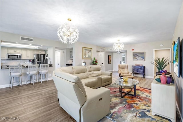 living area with a chandelier, light wood-style floors, visible vents, and baseboards