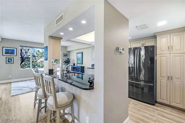 kitchen featuring visible vents, fridge with ice dispenser, a sink, a breakfast bar, and cream cabinetry