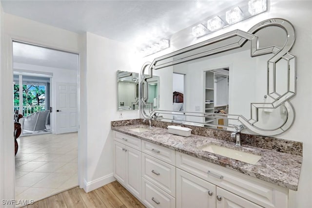 full bathroom featuring a sink, baseboards, double vanity, and wood finished floors
