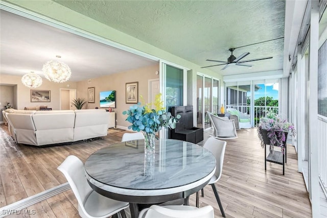 dining space featuring light wood-style flooring, a textured ceiling, and ceiling fan with notable chandelier