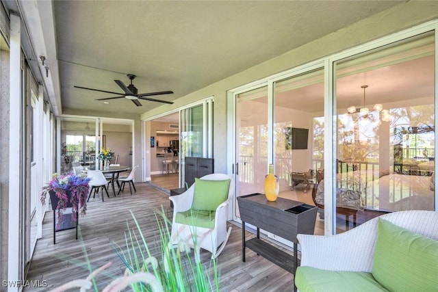 sunroom / solarium featuring outdoor dining space, ceiling fan with notable chandelier, and wood finished floors