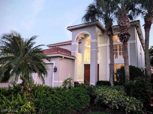 mediterranean / spanish-style house with a tile roof, an attached garage, and stucco siding