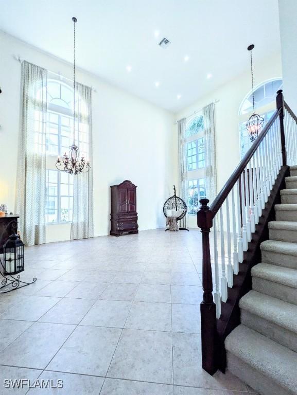 stairway with a towering ceiling, tile patterned flooring, visible vents, recessed lighting, and a chandelier