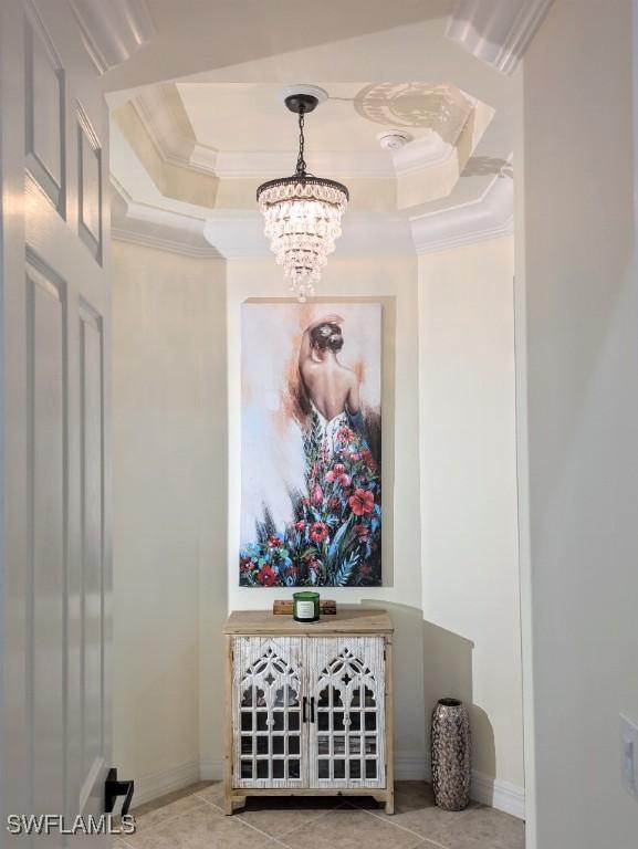 interior space with a tray ceiling, crown molding, an inviting chandelier, and baseboards