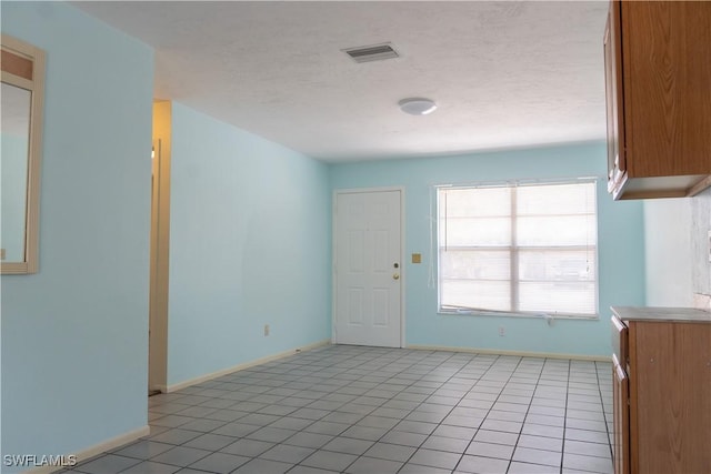 spare room with a textured ceiling, baseboards, visible vents, and light tile patterned floors