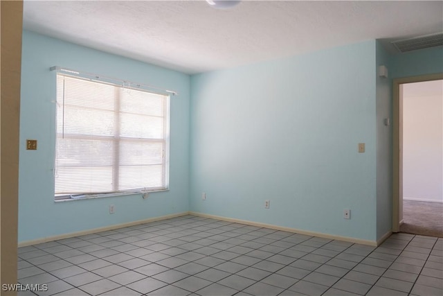 empty room featuring a textured ceiling, baseboards, visible vents, and light tile patterned floors