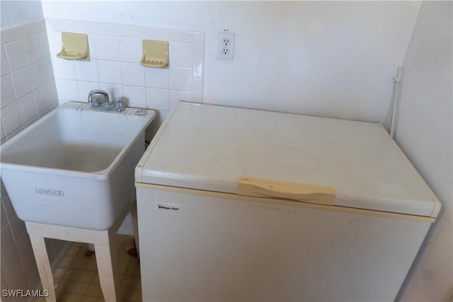 laundry room featuring tile walls and a sink