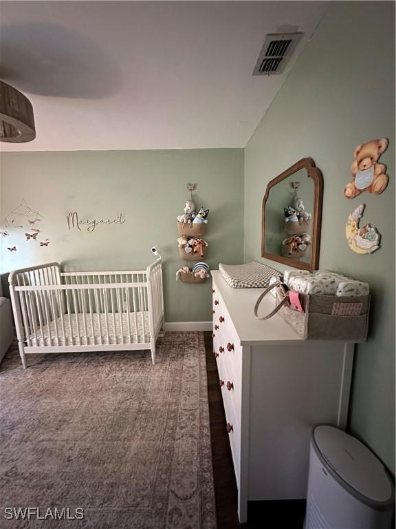 bedroom with visible vents, baseboards, dark carpet, and a nursery area