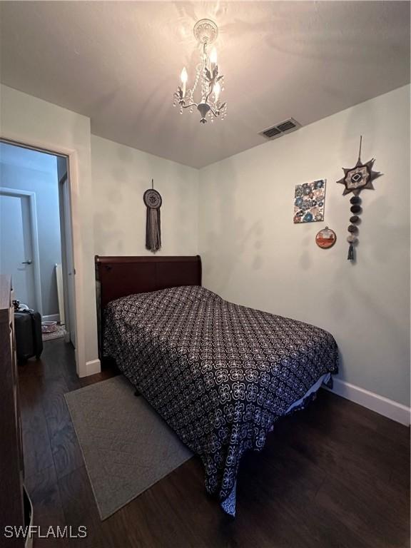 bedroom with visible vents, baseboards, an inviting chandelier, and wood finished floors