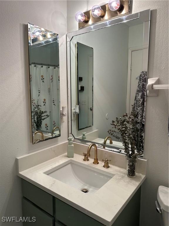 bathroom featuring a textured wall, vanity, a shower with curtain, and toilet