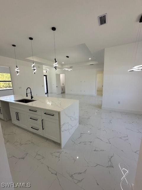 kitchen with an island with sink, light stone counters, visible vents, a sink, and open floor plan