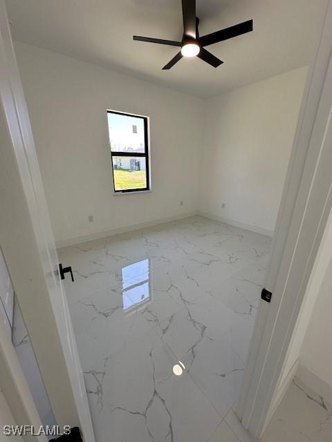 spare room with marble finish floor, baseboards, and a ceiling fan