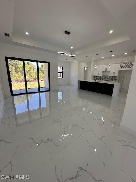 unfurnished living room featuring marble finish floor, baseboards, a tray ceiling, and recessed lighting