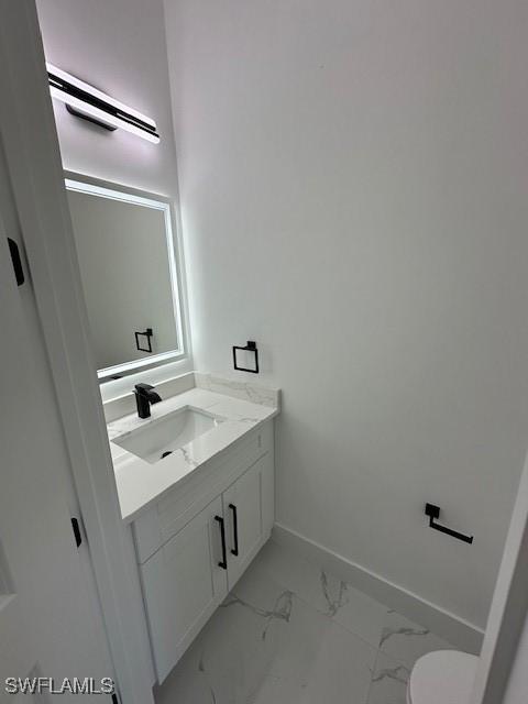 half bath featuring vanity, marble finish floor, baseboards, and toilet