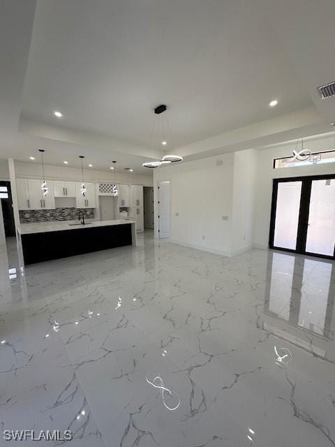 unfurnished living room with a sink, a tray ceiling, baseboards, visible vents, and recessed lighting