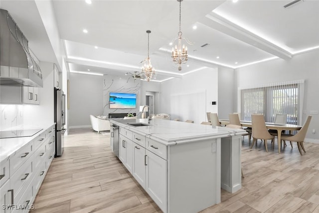 9974 Winterview Dr, Naples, FL 34109 - kitchen featuring wall chimney range hood, a sink, appliances with stainless steel finishes, a chandelier, and a kitchen island with sink