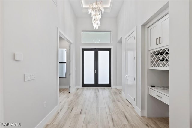 9974 Winterview Dr, Naples, FL 34109 - foyer featuring a chandelier, french doors, a towering ceiling, light wood-style floors, and baseboards