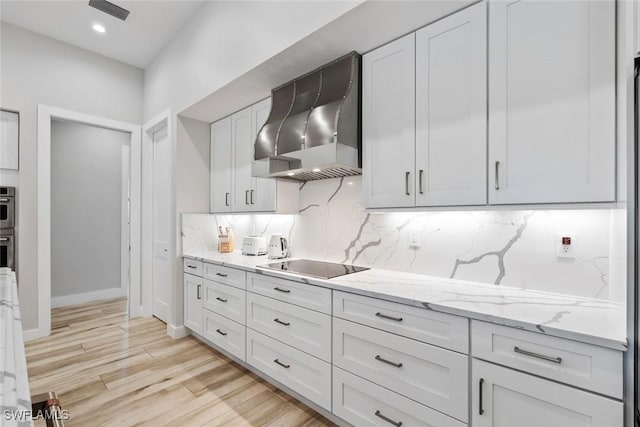 9974 Winterview Dr, Naples, FL 34109 - kitchen with wall chimney range hood, black electric cooktop, decorative backsplash, light wood-style floors, and light stone countertops