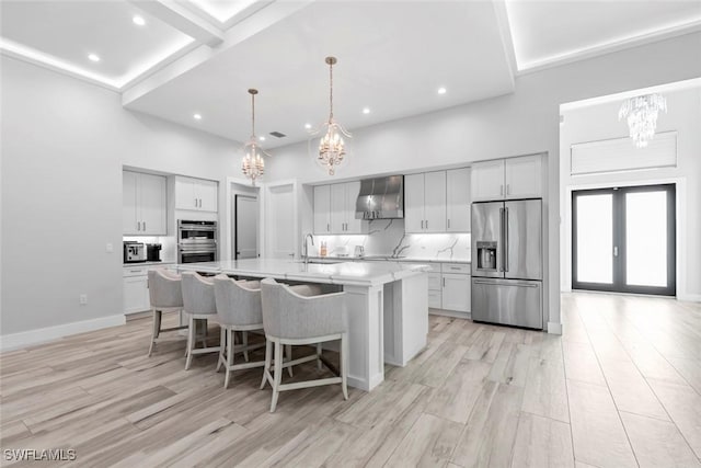 9974 Winterview Dr, Naples, FL 34109 - kitchen featuring stainless steel appliances, a chandelier, wall chimney exhaust hood, light wood finished floors, and a breakfast bar area