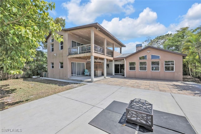 rear view of property featuring a chimney, stucco siding, a patio, and a balcony