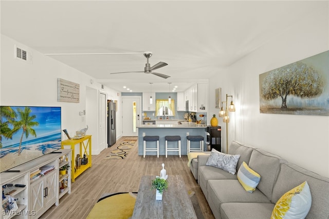 living area featuring light wood-style floors, visible vents, and ceiling fan